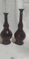 Two tall dark reddish-brown decorative vases with flared necks shown side by side on a white backdrop.