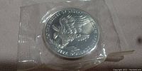 Front side of the silver-colored $5 coin showing an eagle and inscriptions honoring Desert Storm heroes, sealed in plastic.