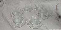 Six clear glass espresso cups paired with their matching six clear glass faceted saucers arranged on a surface.