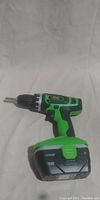Side view of the Kawasaki 21.6V cordless drill standing upright, showing green and black plastic body and battery pack attached at the bottom.