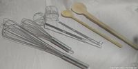 Photo of metal whisks, wooden spoons, and long-handle wire skimmers showing utensil design and size.