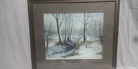 Full view of the framed watercolor painting showing a winter landscape with trees and a stream.
