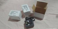 Two white boxes and one power supply adapter with cord on a pink fabric surface