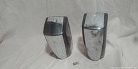 Two chrome soap dispensers placed side by side on a light cloth background with a small key in front.