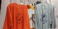 Front view of three different sport shirts hung on hangers against a white backdrop, left shows orange knit shirt with maple leaf '67' design, middle shows white hockey jersey with tiger, right shows gray shirt with Crate logo.