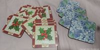 Set of 15 vintage square coasters arranged in two groups on a light surface, showing holly and floral designs.