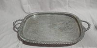 Top view of rectangular silver engraved serving tray with two handles and border decoration. Shows surface wear and tarnish.