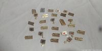 Overview of 29 vintage MIHCK pin badges laid out on a white cloth showing various rectangular designs with gold finish and red enamel accents.