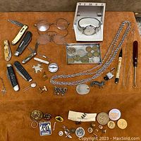 Full collection of items arranged on a surface showing knives, glasses, watch box, chains, coins, cufflinks and small memorabilia.