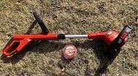 Full view of Black & Decker cordless string trimmer lying on the ground with a roll of replacement string next to it.