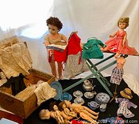 Overall view showing vintage dolls, doll clothes in cloth cases, tea set, and child's ironing board.