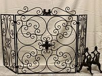 Front view of the decorative wrought iron fireplace or garden gate with intricate swirl patterns and bird accents.