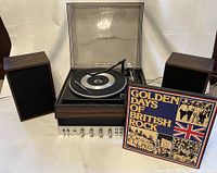 Turntable with plastic dust cover, speakers, and Golden Days of British Rock LP box set displayed together