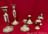 Overall view of two pairs of sterling silver candleholders and a pair of salt and pepper shakers set against a red background.
