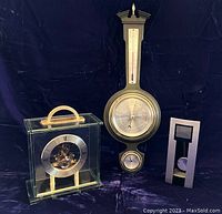 Set of three items against dark background: ornate banjo style weather station, clear glass Seiko mantle clock, and small pendulum clock