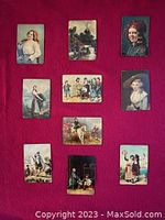 Photo showing all 10 glazed metal plaques on red fabric background, variety of portrait, landscape and folk scenes visible