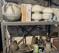 Shelf with large vintage pressed glass ceiling light covers with white and some blue painted details, assorted smaller lamps including a vintage brass hanging lamp, and a used wall sconce with glass shade boxed