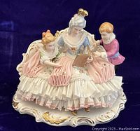 Front view of the porcelain figurine showing the mother and two children seated, highlighting the lace dress and gold accents.