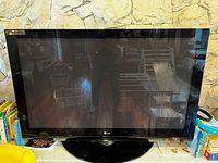 Front view of LG 50-inch television on black stand against stone wall with various household items around.