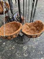 Two metal hanging flower baskets with brown coco liners, hanging from metal frame