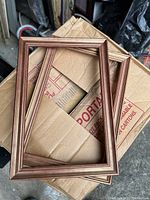 Wooden photo frames stacked on a cardboard box, showing brown frames with a beaded decorative edge.