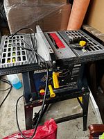 Mastercraft 10 inch table saw with stand, power cord, push stick and push block accessory on top, showing front view with brand name and controls visible.