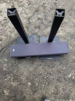Photo showing the two black metal speaker stands and the gray center channel speaker resting between them.
