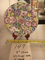 Front view of the 8-inch vintage Chinese porcelain plate on the wooden stand with ruler for size reference.