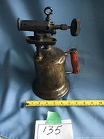 Antique brass/copper gas blow torch showing side view with red handle and gas nozzle.