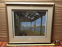 Framed artwork showing a porch scene with four men and a distant church across water under a partly roofed porch, triple matted and behind glass.