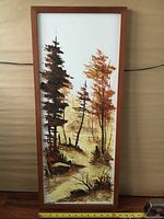 Full view of framed vertical oil painting depicting autumn trees and a cabin in the background.