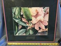 Frontal photo of framed watercolor painting showing pink flowers and green leaves with measuring tape for scale, showing frame dimensions.