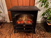 Front view of black metal stove fireplace showing arched glass front with glowing ember logs