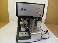 Front view of Oster espresso maker showing portafilter, drip tray, and side water tank