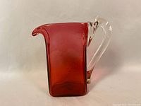 Front and side view of red Depression glass decanter with clear handle and pouring spout, showing square shape and color.