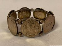 Image showing oval silver coins with detailed engravings connected by silver frame beads. One coin has the inscription 'Nancy'.