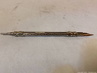 Full view of silver mechanical antique pencil laid flat showing engraved design and tip.