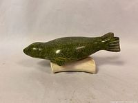 Side view of green soapstone seal figurine lying on white base showing shape and condition.