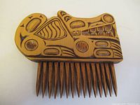 Front view of wooden hair clip showing stylized wolf carving in First Nations design.