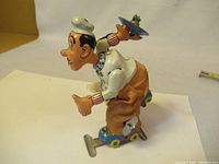 Side profile of the vintage toy showing the chef in mid-skate position holding a plate, colorful painted tin with fabric pants and roller skates.