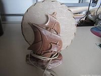 Front view of vintage sailing ship ceramic lamp base and round fabric lampshade with gold trim.