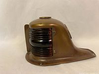 Side profile of the solid brass vintage boat light showing the black ribbed glass lens and the brass mounting base with holes for screws.