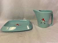 Front view of light blue ceramic pitcher and rectangular base, each featuring Johnny Walker striding man in red jacket and slogan.