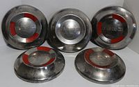 Set of five Ford car hubcaps displayed showing front sides, three with red accent around "FORD" lettering.