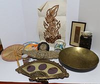 Full lot overview showing all items including carved wooden angel wall decor, brass tray, fan frame, bamboo fan, ceramic planter, plates, cup, and Asian print.