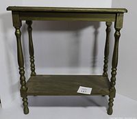 Front view of green wooden side table showing turned legs, top surface, and lower shelf