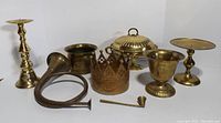 Photo showing full lot of brass items including candlesticks, horn, crown, snuffer and other vessels