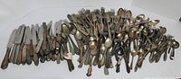 Overview of the entire utensil lot showing knives, forks, and spoons arranged on a white surface with visible tarnish and vintage wear.