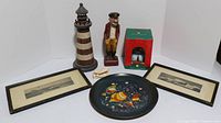 Wide view of all nautical items including lighthouse, sea captain figurine, framed seascapes, fish plate, water globe, and crab decor piece arranged on table.