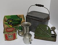 Group photo of the lot showing the pewter trumpet mug, small pewter cup, green egg scale, Slade's caramel toffee tin, vintage metal lunch box, and Ertl John Deere tractor toy in original box.